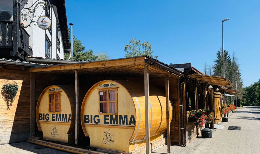 Außenansicht von BIG EMMA in Ramstein-Miesenbach mit holzverkleideter Almhütte und großen Fässern mit Firmenaufdruck